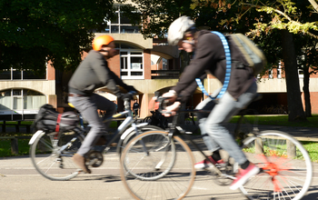 Two cyclists breezing through the ɫ campus on a sunny day